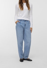 Světle modré džíny s vysokým pasem, volného střihu, s předními záhyby, bočními kapsami a rovnými nohavicemi. Kombinované s bílým topem s dlouhým rukávem.