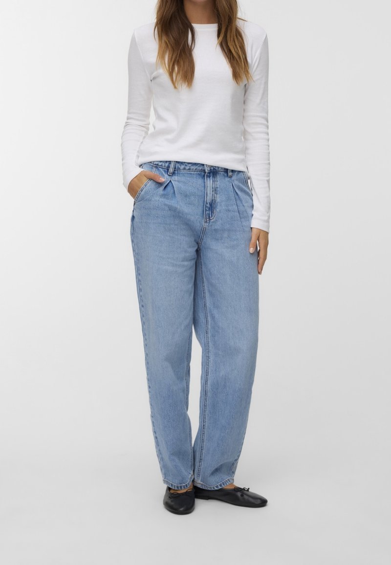 Světle modré džíny s vysokým pasem, volného střihu, s předními záhyby, bočními kapsami a rovnými nohavicemi. Kombinované s bílým topem s dlouhým rukávem.
