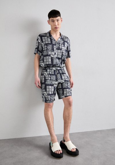 Short-sleeve button-up shirt and matching shorts in dark blue with floral and geometric patterns; paired with chunky, cream-colored sandals.