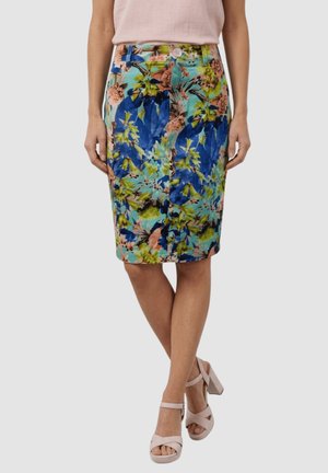 Mujer que lleva una falda hasta la rodilla con un patrón floral colorido en azul, verde y rosa, combinada con una blusa sin mangas rosa pálido y tacones rosa claro.