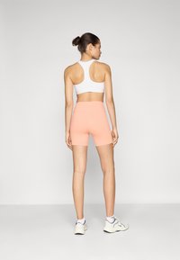 White racerback sports bra, peach high-rise shorts, smooth texture, fitted design, and athletic shoes with a light gray and black color scheme.