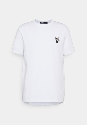 Weißes Baumwoll-T-Shirt mit rundem Halsausschnitt und kurzen Ärmeln, das auf der linken Brust ein kleines schwarzes Cartoon-ähnliches Figur zeigt.