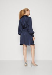 Navy blue satin dress with a collar, long puff sleeves, tie belt at the waist, and a flared skirt. Glossy silver high-heeled shoes.