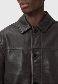 Veste en cuir marron avec une finition texturée, dotée d'un col, de quatre boutons de fermeture et de détails de couture visibles.