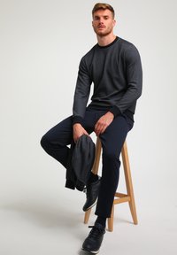 Mørkegrå herresweatshirt med sorte detaljer, paired med marineblå bukser. Model siddende på en træstol, holder en matchende jakke.