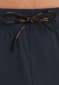 Shorts de bain bleu marine avec taille élastique, dotés d'un cordon de serrage avec texte de marque et embouts en plastique noir, et panneau avant à double couture.
