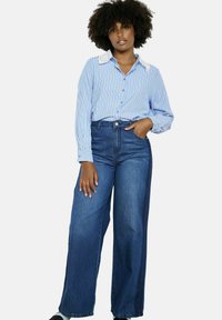 Lichtblauw en wit gestreepte blouse met een kantkraag, gecombineerd met hoge taille, wijde, donkerblauwe jeans.
