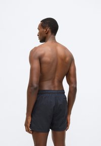 Juodi maudymosi šortai su elastiniu liemeniu ir galine kišene. Audinys atrodo lengvas ir lygus, tinkamas vandens veikloms.