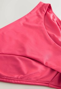 Fuksia ujumisriiete ülemine osa, millel on sile ja veniv tekstuur. Omab V-kujulist kaelust ja diskreetset õmblust servade ümber.