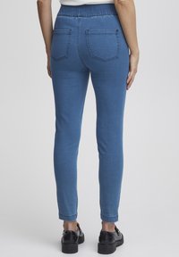 Pantalones de mezclilla elásticos azules con cinturilla alta, corte ajustado, dos bolsillos traseros y una textura suave.