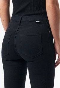 Černé džíny slim fit s zadními kapsami a středním pasem. Hladká, texturovaná tkanina s minimálním prošíváním a štítkem značky.