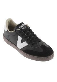 Svart och vit sneaker med en texturerad mockafront, slät läderkropp, rund tå och platt gummisula. Har snörning och logotypdetalj.