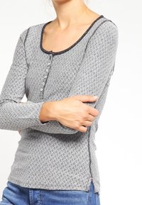 Long-sleeve shirt in gray with a diamond pattern, scoop neck, button closure, and black trim along the neckline and cuffs.