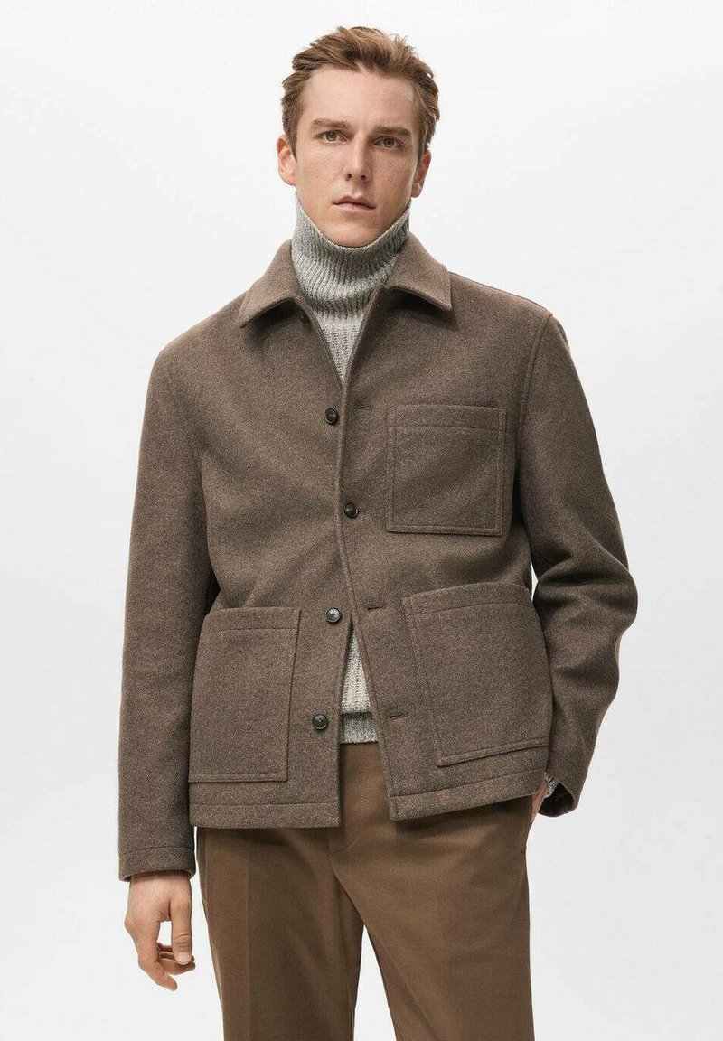 Braune Jacke aus Wollmischung mit einem Kragen, zwei Fronttaschen und Knopfverschluss. Getragen über einem grauen Rollkragenpullover.