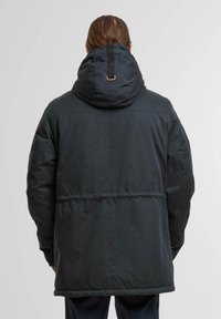 Veste noire matelassée avec capuche. Présente une taille cintrée, une sangle au dos et un tissu lisse avec une finition mate. Couture renforcée visible.