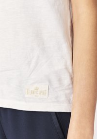 Camiseta blanca hecha de un tejido ligero, con una textura sutil y una etiqueta de tela con la marca "ATLANTIC SPIRIT" en el dobladillo.