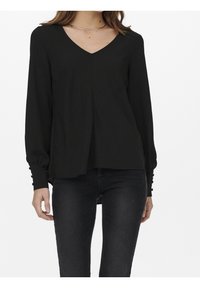 Schwarze Bluse mit V-Ausschnitt, langen Ärmeln, strukturiertem Stoff und Knopfakzenten an den Manschetten. Das Design hat einen lockeren, fließenden Schnitt.