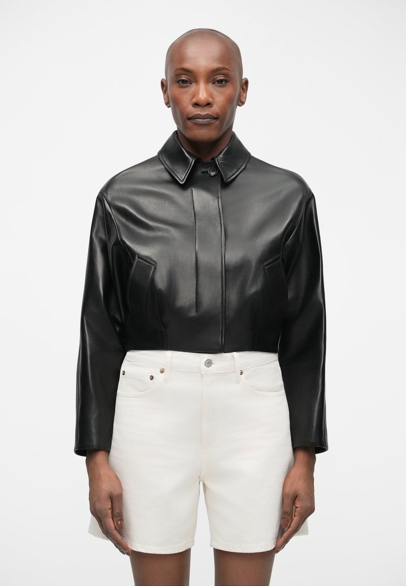 Must tume nahk jakk kraeppidega, millel on ees seam detailid, koos valgete denim lühikestega. Puhas disain ja sile tekstuur.