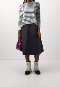 Gestreifter Langarm-Oberteil, gesteppter dunkler Rock, weiße und schwarze Winterstiefel und eine kleine glänzende rosa Handtasche.
