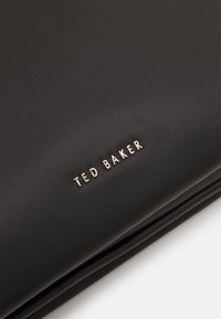 Svart skinnlommebok med en strukturert overflate, med trykt "TED BAKER"-merke i gull. Rektangulær form med rene kanter.
