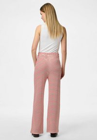 Pantalons large rayés rouge et blanc avec une taille élastique, fabriqués en tissu doux ; associés à un débardeur blanc ajusté.