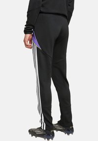 Schwarze Sporthose mit drei weißen Streifen an den Seiten, mit lila und gelben Akzenten, gefertigt aus glattem, elastischem Material.