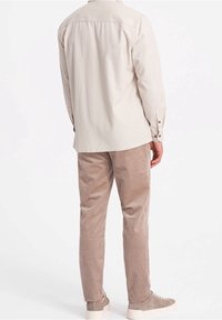 Camisa beige de manga larga con botones, combinada con pantalones de pana color coñac y zapatillas deportivas gris claro, vista desde atrás.