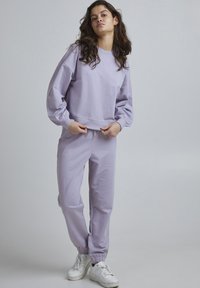 Felpa lilla e pantaloni abbinati realizzati in tessuto morbido. La felpa presenta un collo a giro e maniche a palloncino. Polsini elastici sui pantaloni.