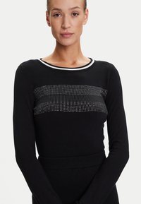 Maglione nero a maniche lunghe con una fascia orizzontale testurizzata di accenti argentati. Collo e vita a coste. Tessuto liscio, design aderente.
