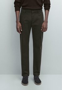 Pantaloni verde scuro con una vestibilità dritta, due tasche laterali e chiusura con bottone frontale, abbinati a scarpe scure. Tessuto morbido al tatto.