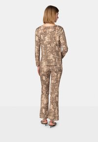 Top a maniche lunghe con stampa serpente beige e marrone e pantaloni a zampa abbinati, realizzati in tessuto morbido, con una vestibilità rilassata e un colletto discreto.