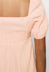 Vestido rosa de mangas bufantes com corpete pregueado e tecido texturizado. Apresenta um decote quadrado e uma bainha em camadas e rodada.