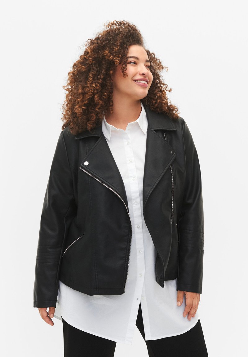 Veste de motard en cuir noir synthétique avec une fermeture éclair asymétrique, un col à revers et des détails côtelés sur les manches, superposée à une chemise blanche.