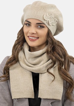 Berretto beige lavorato a maglia con un accento floreale, abbinato a una soffice sciarpa coordinata. Entrambi sono realizzati in un tessuto caldo e strutturato.