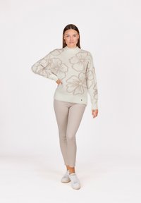 Pull vert clair avec un motif floral beige, col rond et manches longues, associé à un pantalon skinny beige et des baskets blanches.