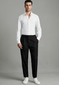 Chemise blanche à manches longues avec col boutonné, associée à un pantalon noir ajusté et des baskets blanches. Design simple, coupe ajustée.