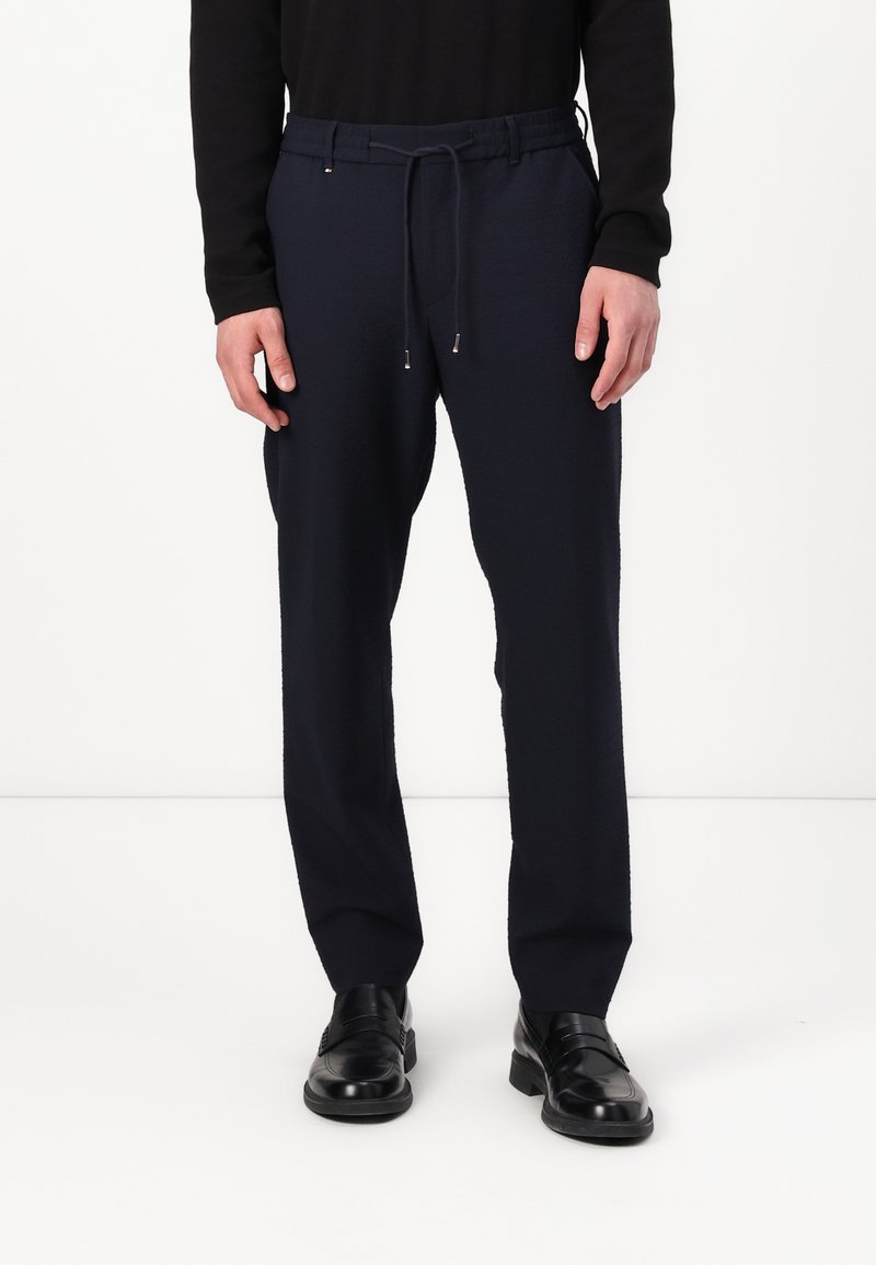 Pantaloni negri cu croi lejer, dotati cu talie elastica, cordon ajustabil si buzunare laterale. Textura neteda, fara modele vizibile.