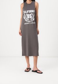 Robe grise sans manches en coton, avec un col rond et une coupe jusqu'aux genoux. Présente une impression graphique blanche indiquant "CALIFORNIA 95".