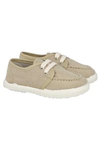 Zapatillas de lona beige presentan un diseño redondeado, con suelas de goma blancas y dos cordones elásticos. La parte superior tiene detalles cosidos y un acabado texturizado.