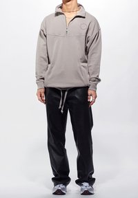 Šedý fleecový pulovr se čtvrtinovým zipem vpředu, s jemným logem a volným střihem, kombinovaný s černými hladkými koženými kalhotami.