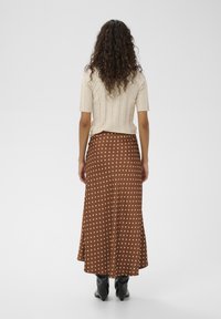 Brun nederdel med polkaprikker og flæset kant, lavet af glat stof, kombineret med en beige, ribstrikket top med korte ærmer. Sorte ankelstøvler er synlige.