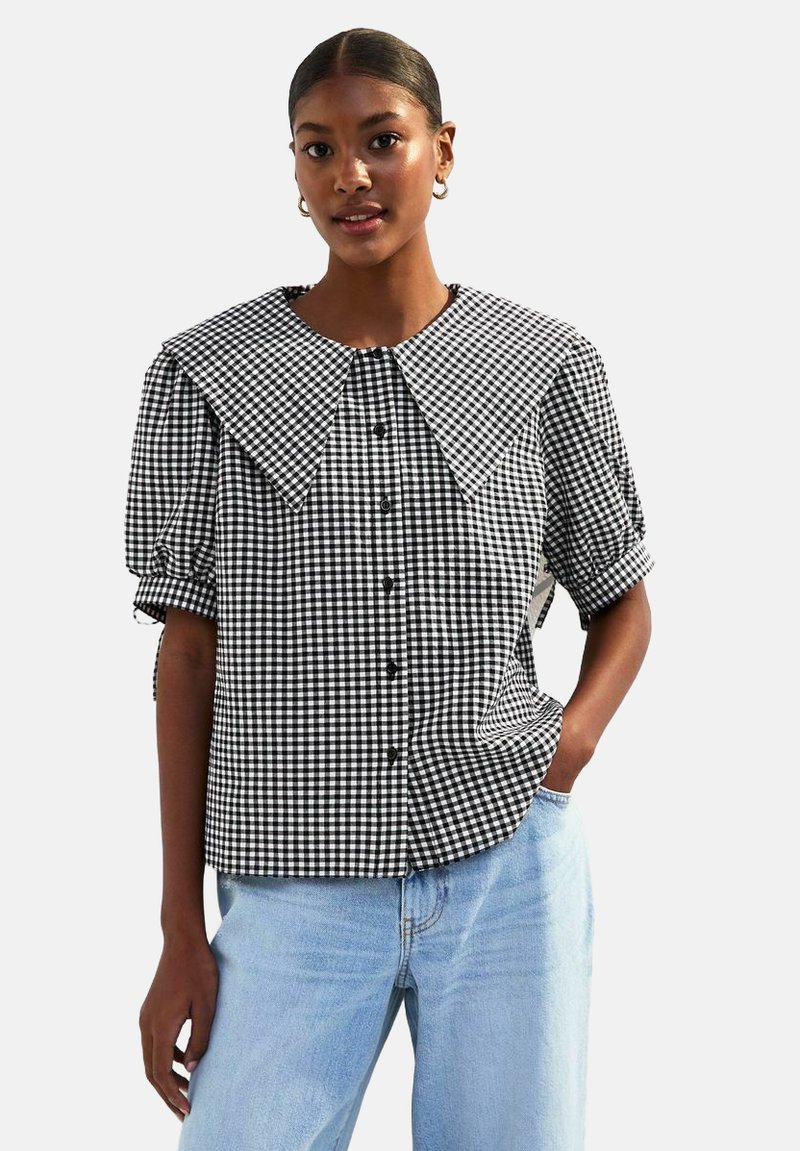 Svartvitrutig blus med stor krage, puffärmar, knappstängning och avslappnad passform, tillsammans med ljusblå jeans.