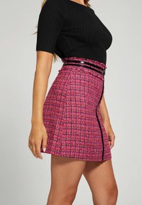 Lyserød tweed nederdel med et struktureret mønster, der har en kontrasterende sort lynlås og en blank sort talje. Kort længde og tætsiddende design.