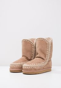 Tan suede ankelstøvler med blødt indre for, indviklet syning langs sømmene og flade gummisåler. Enkel, afrundet design.