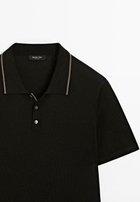 Sort polo-shirt med en kontrasterende lys grå krave. Har tre knapper på placket og korte ærmer. Fremstillet af et glat, strikket stof.