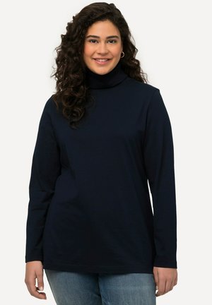 Camisa de cuello alto de manga larga en color marino, fabricada con material suave, con un corte relajado y un diseño de cuello sin costuras, acompañada de jeans de color azul claro.