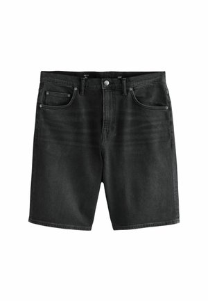 Ein Mann steht auf Gras, trägt ein lila "Venice Beach Hip Hop" T-Shirt, schwarze Shorts, schwarze Socken und weiße Sneakers und schaut nach links.