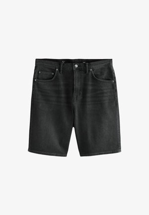 Hombre de pie sobre el césped con una camiseta morada «Venice Beach Hip Hop», pantalones cortos negros, calcetines negros y zapatillas blancas, mirando hacia la izquierda.
