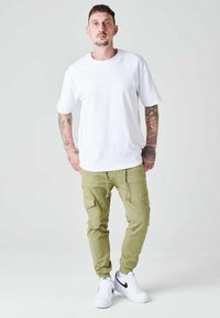 Camiseta blanca de algodón combinada con pantalones cargo verde olivo, que presentan bolsillos laterales y puños en los tobillos. Completo con zapatillas blancas.