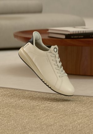 Hvit skinnsneaker med avrundet tå, snøring foran og kontrasterende mørk hæl. Teksturert såle med fleksible spor for grep og komfort.